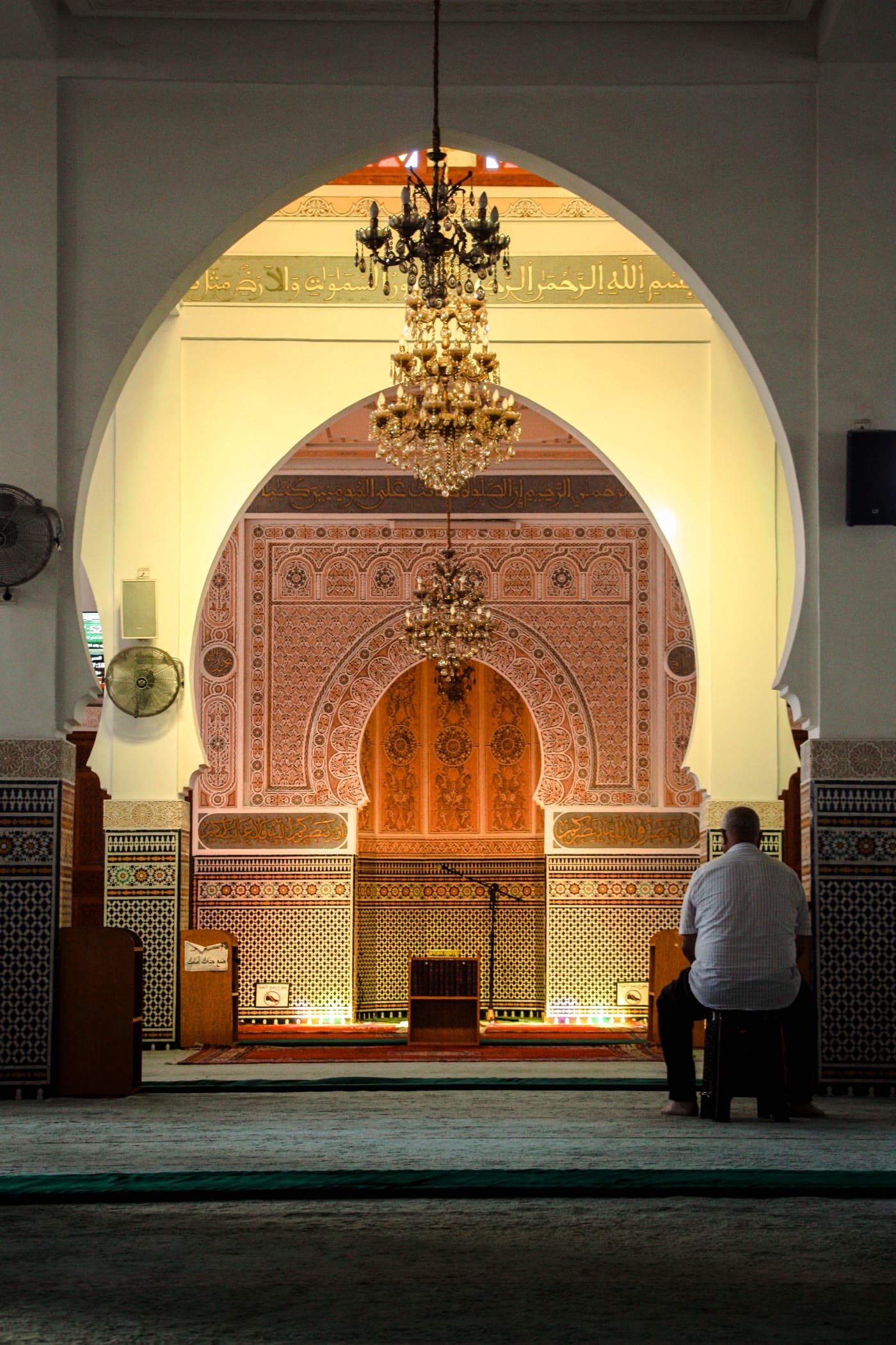 A tiled mosque mihrab beneath a crystal chandelier