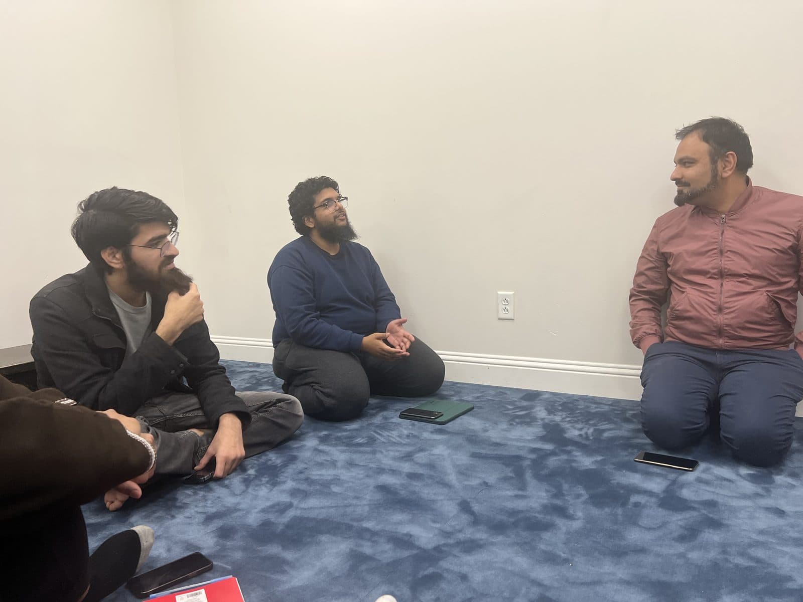 Three men in quiet conversation seated on the floor