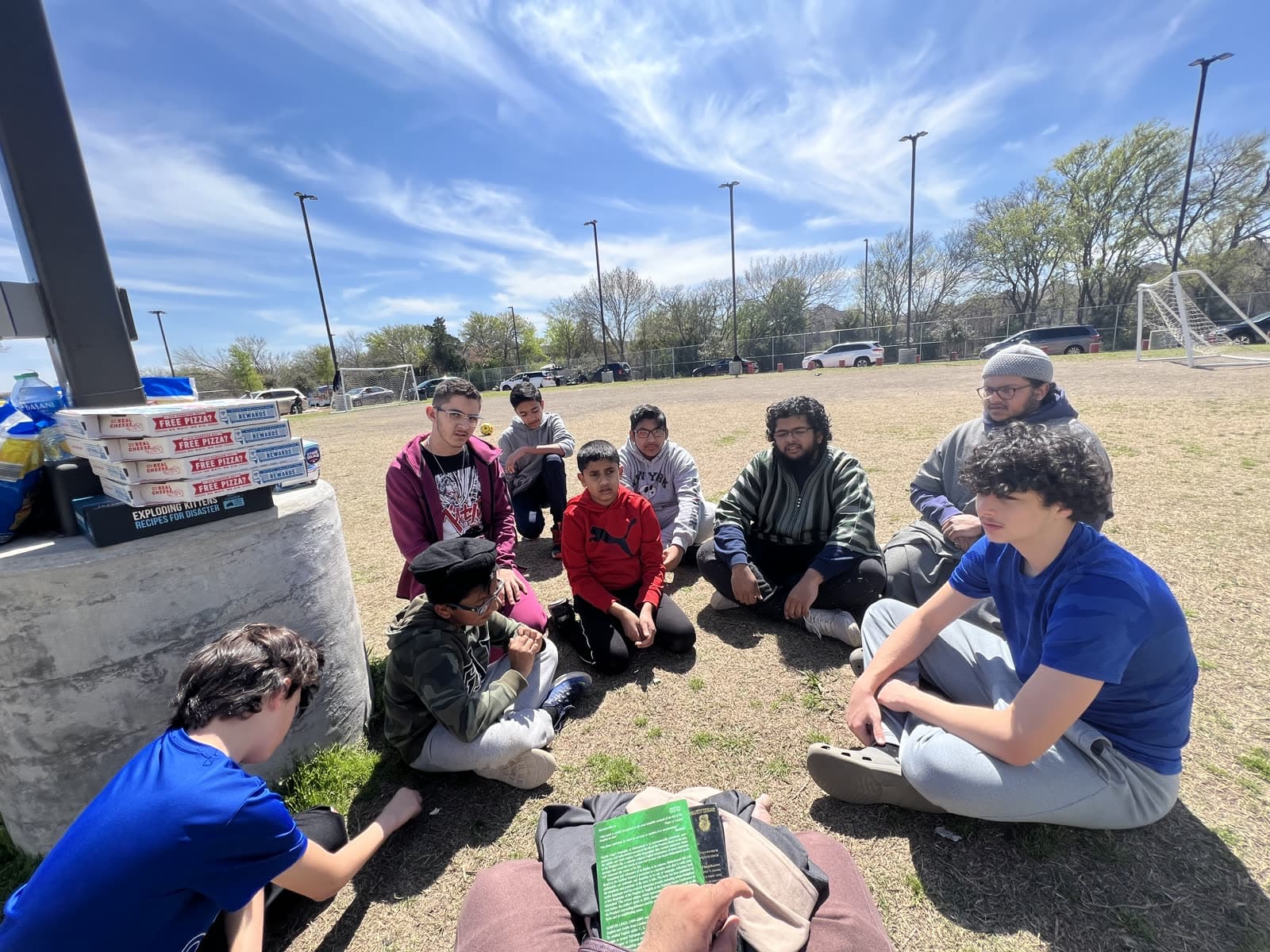 Teenage boys sitting on the grass in a circle listening as their mentor reads from a book