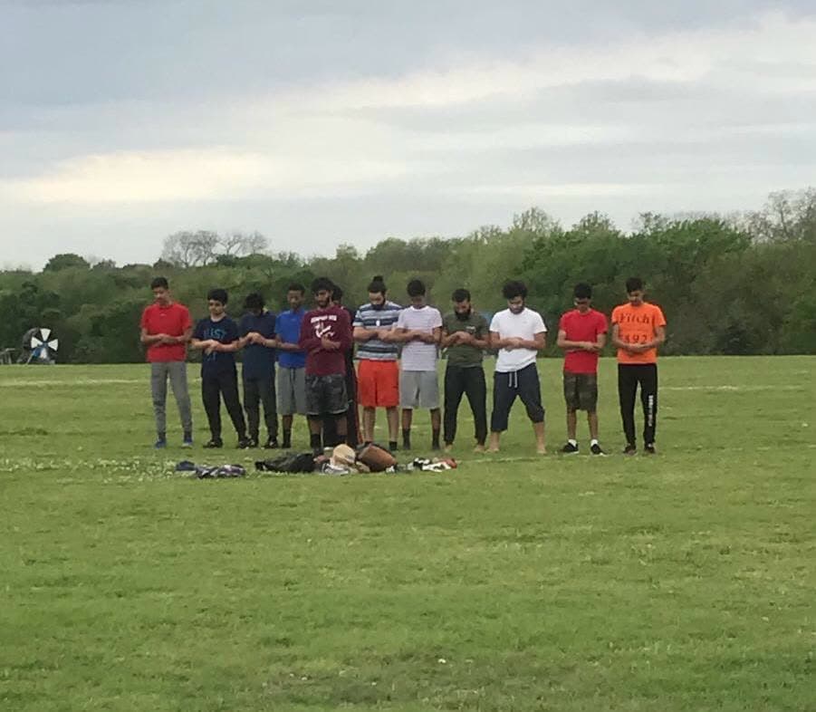 A row of young men standing shoulder to shoulder in prayer in an open field