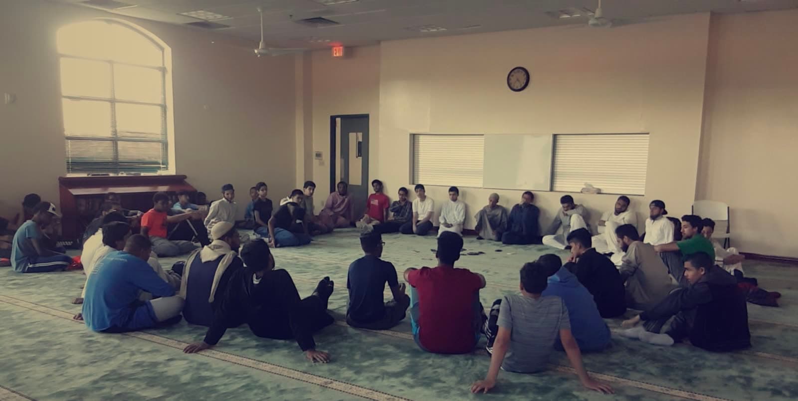 Roughly thirty-five young men sitting in a circle on a masjid floor during a halaqah
