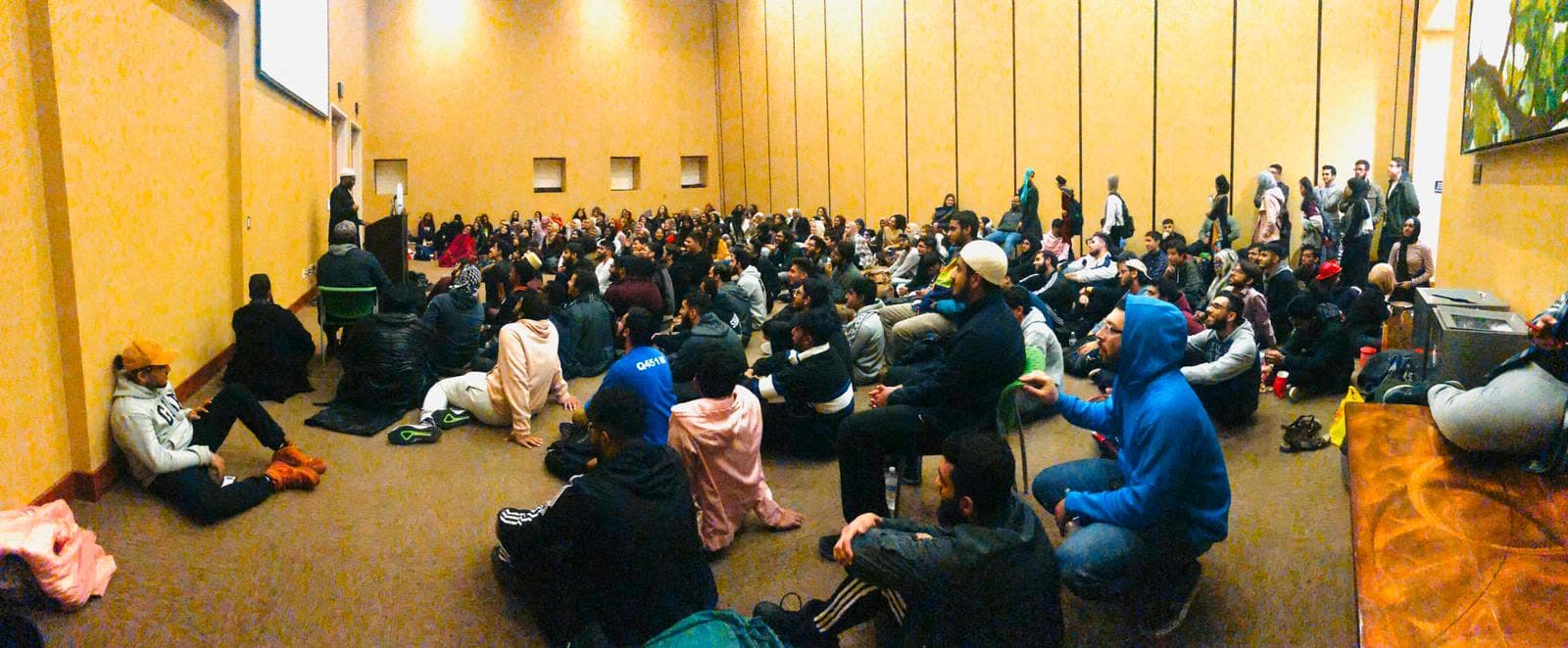 A room packed wall to wall with young people seated on the floor for a program