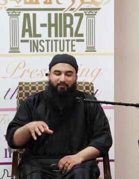 Irslan teaching, seated in front of an Al-Hirz Institute banner