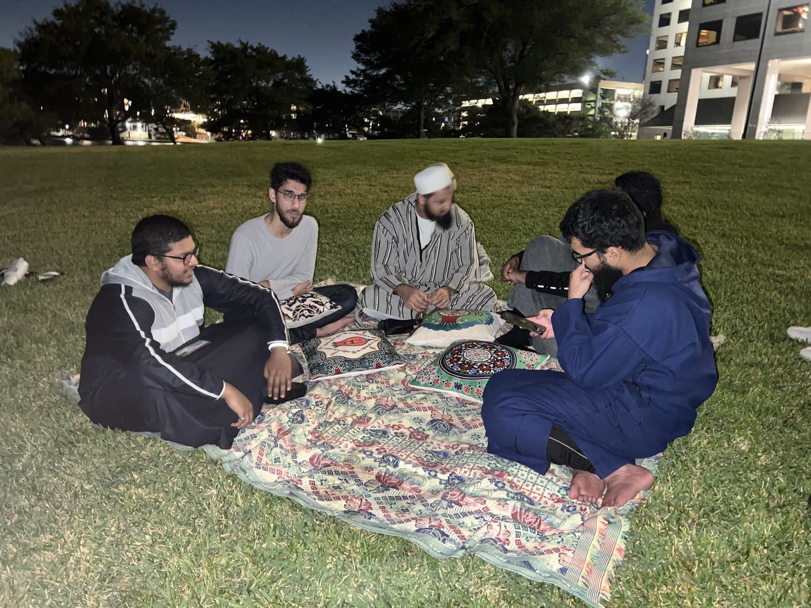 A late-night circle of friends gathered on a picnic blanket outdoors