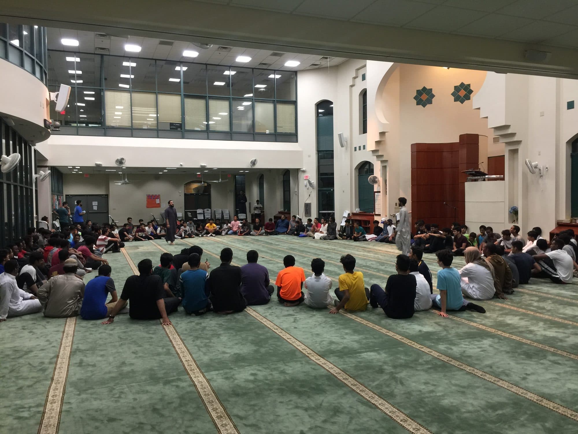 A large circle of students seated in a grand mosque hall at night