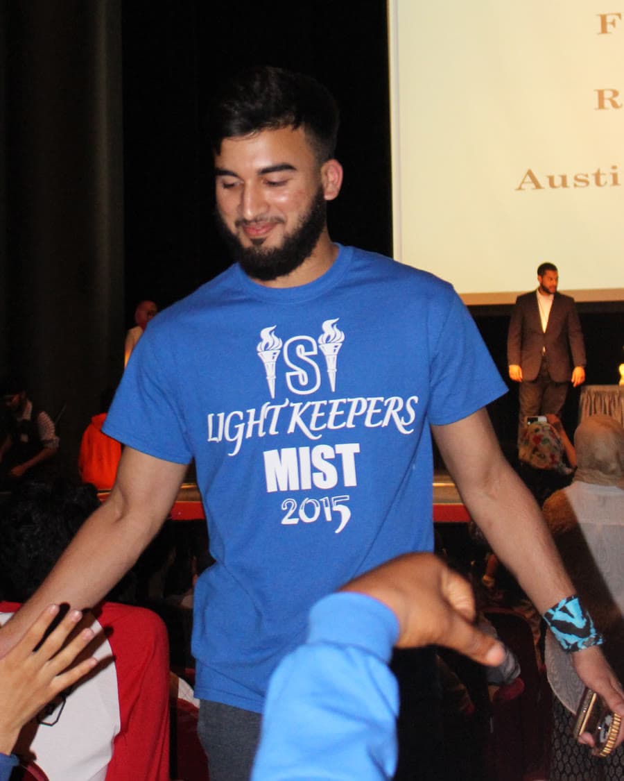Irslan in a Light Keepers MIST 2015 shirt walking through an auditorium, hands reaching out to meet his