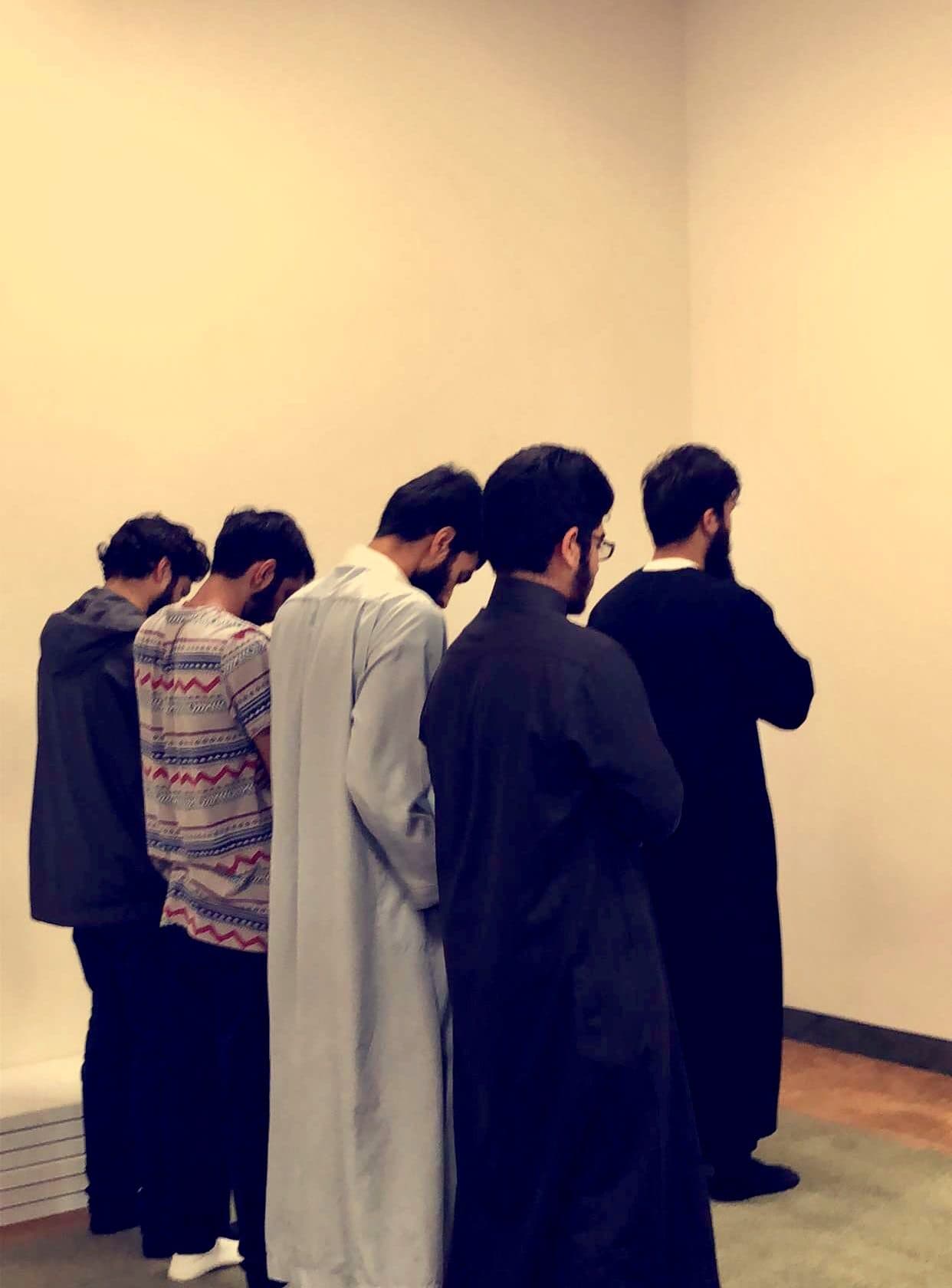 Five men standing shoulder to shoulder in prayer, seen from behind