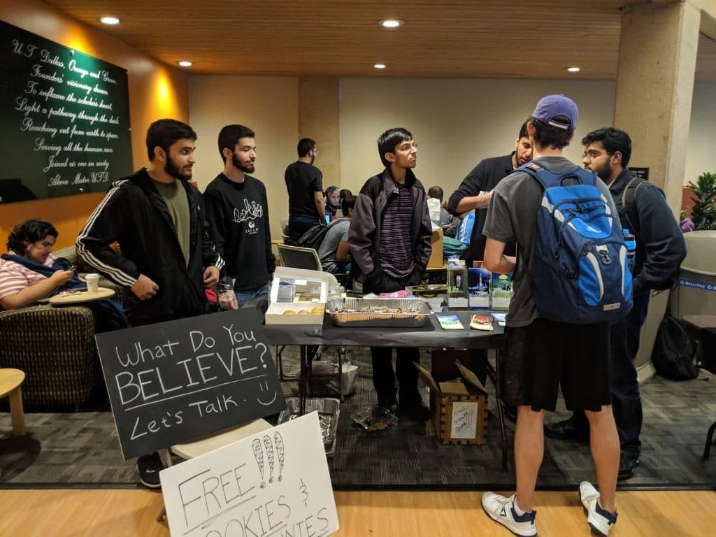 A campus outreach table with a sign reading 'What Do You Believe? Let’s Talk’
