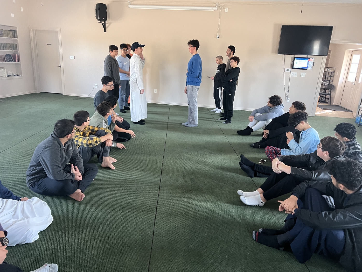 Students standing to present while the rest of the circle sits listening around the hall